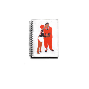 Caderno de bolso com capa em tons de vermelho e fundo branco e wire-o branco com ilustração de casal de homem negro e mulher negra de pé, trajando roupas em tons de vermelho. O caderno de bolso pra quem ama o dengo.
